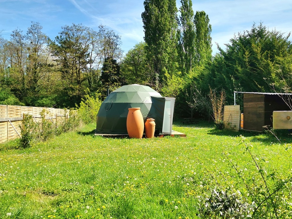 Vue romantique du Dôme de l’Aube dans un jardin de pommiers, un cadre paisible pour un séjour intime.